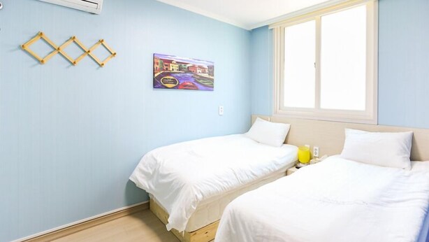 A room with two beds, a window, an air conditioner, and a painting on the wall. - Beluga Guest House - Hostel (Yeosu)