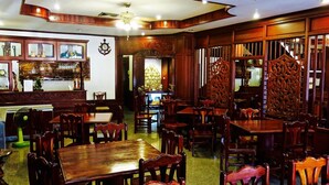Un décor intérieur traditionnel en bois, avec de nombreuses tables et chaises, un coin bar doté de vitrines et un mur décoratif orné d’une horloge et d’un motif d’ancre.