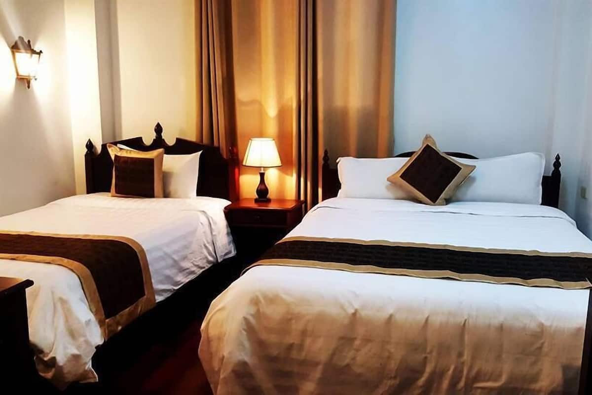 Dos camas individuales con cabeceros de madera, una mesita de noche con lámpara, y una lámpara de pared.