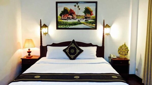 A neatly made bed with a decorative pillow, two bedside lamps, and a framed painting above the bed. - Khampiane Boutique Hotel (Vientiane)