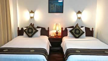 A hotel room with two single beds, each with a decorative pillow and a nightstand with a lamp.