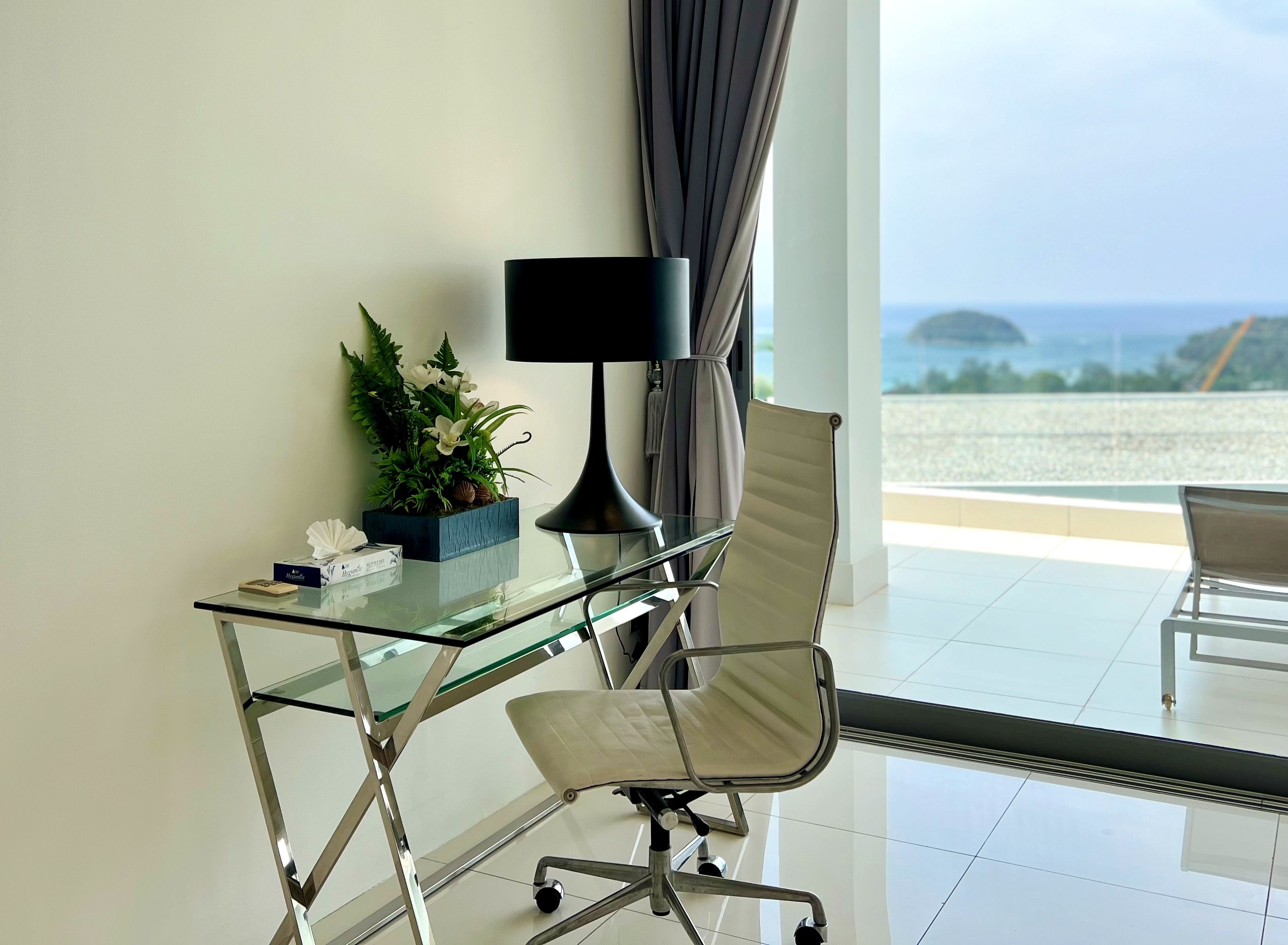 Un espacio de oficina moderno con un escritorio de vidrio, una lámpara negra, una silla acolchada y una planta en maceta.