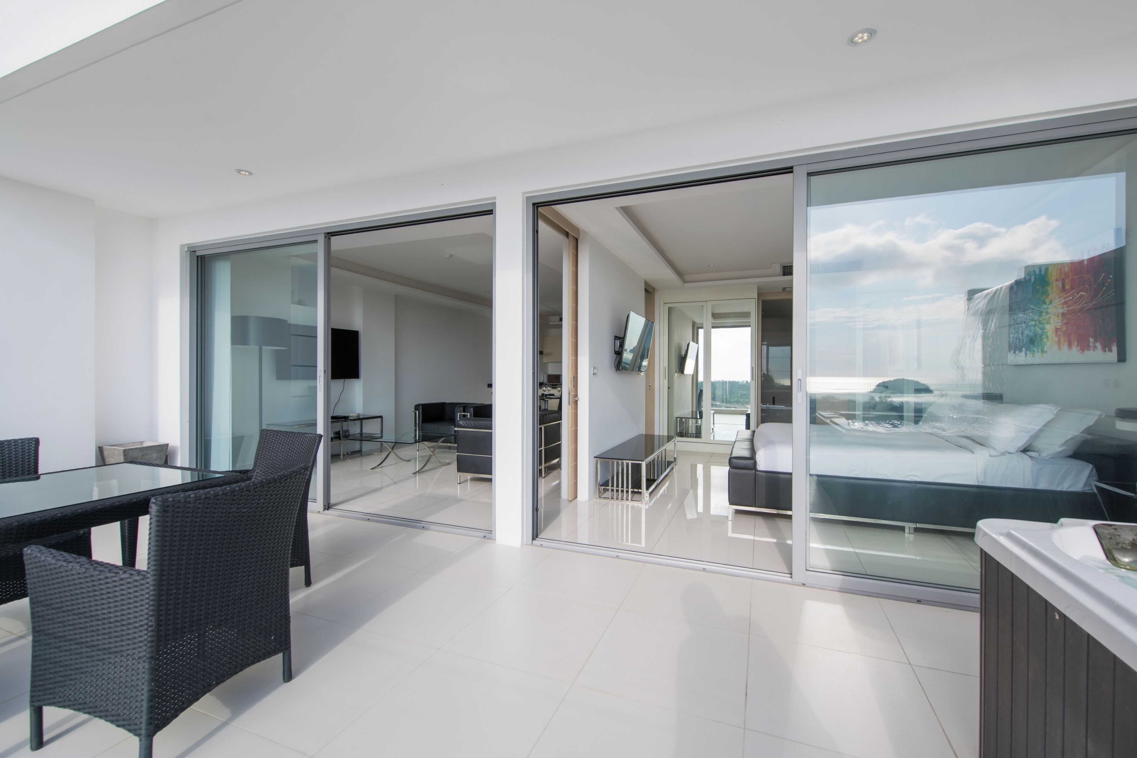 A modern hotel room with a glass wall, a dining area with a table and chairs, and a bed with a view.