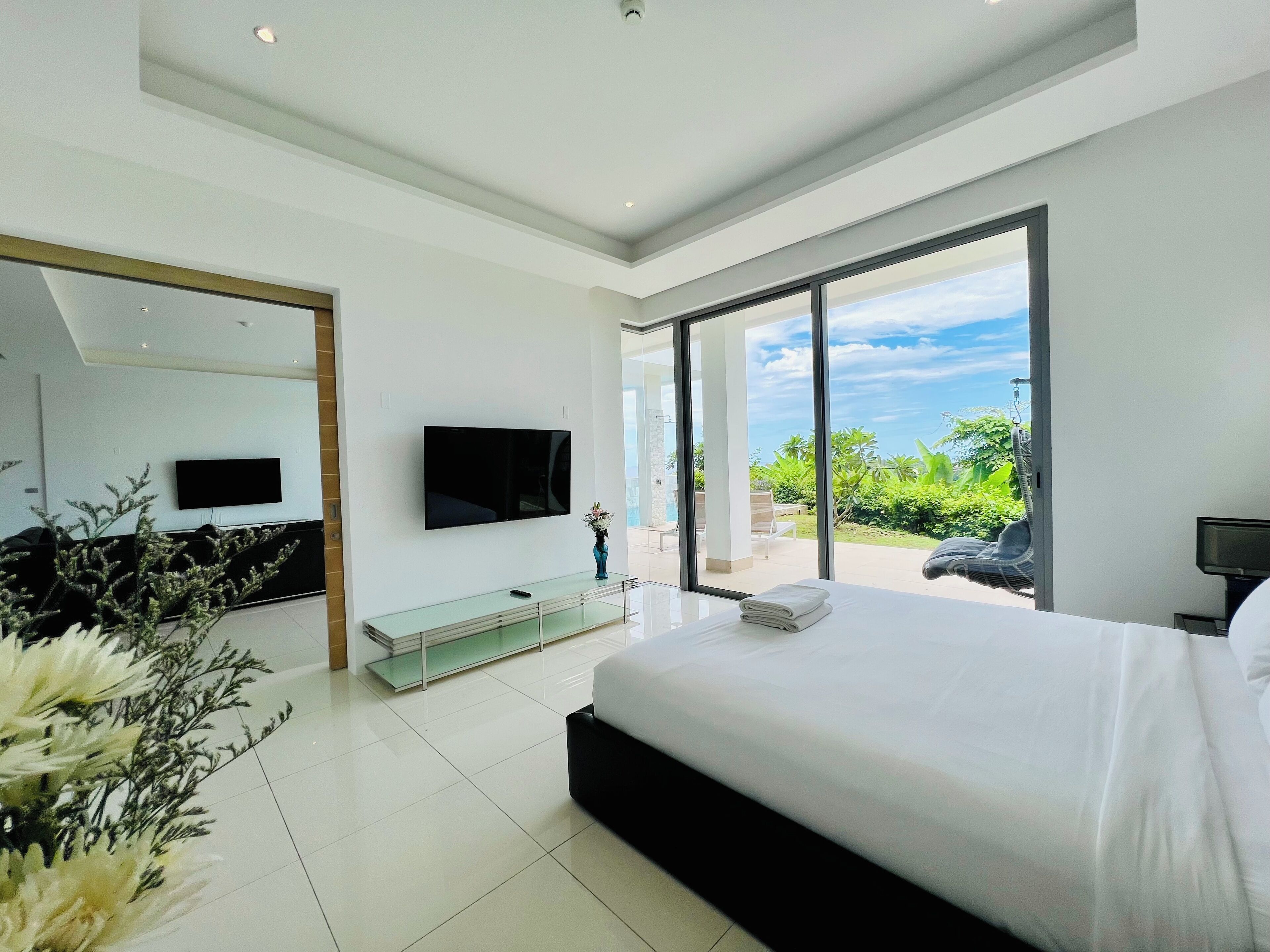 A modern bedroom with a large bed, a flat-screen TV, and a glass coffee table.