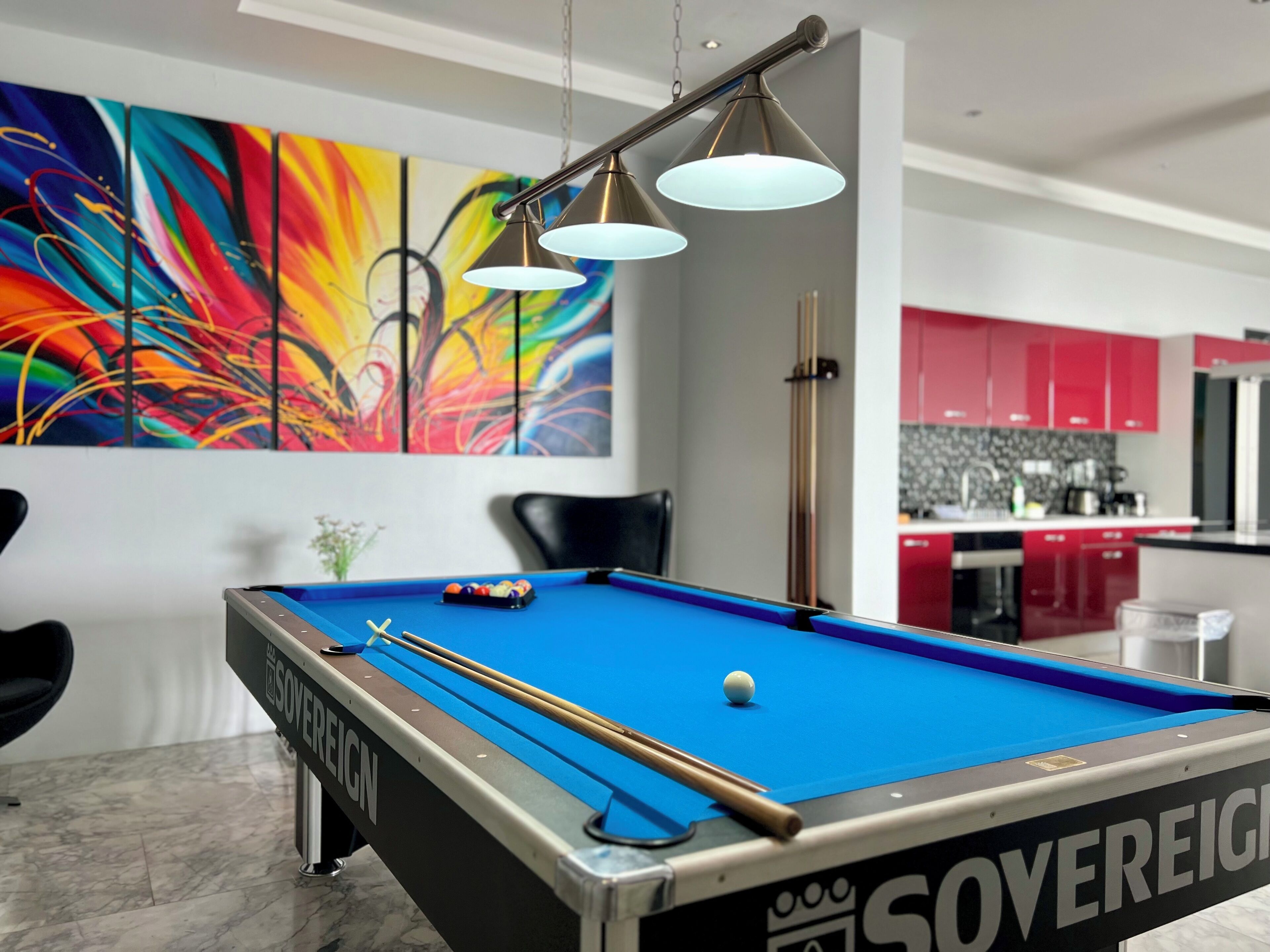 A pool table with a "Sovereign" label, a colorful abstract painting, and a modern kitchen in the background.