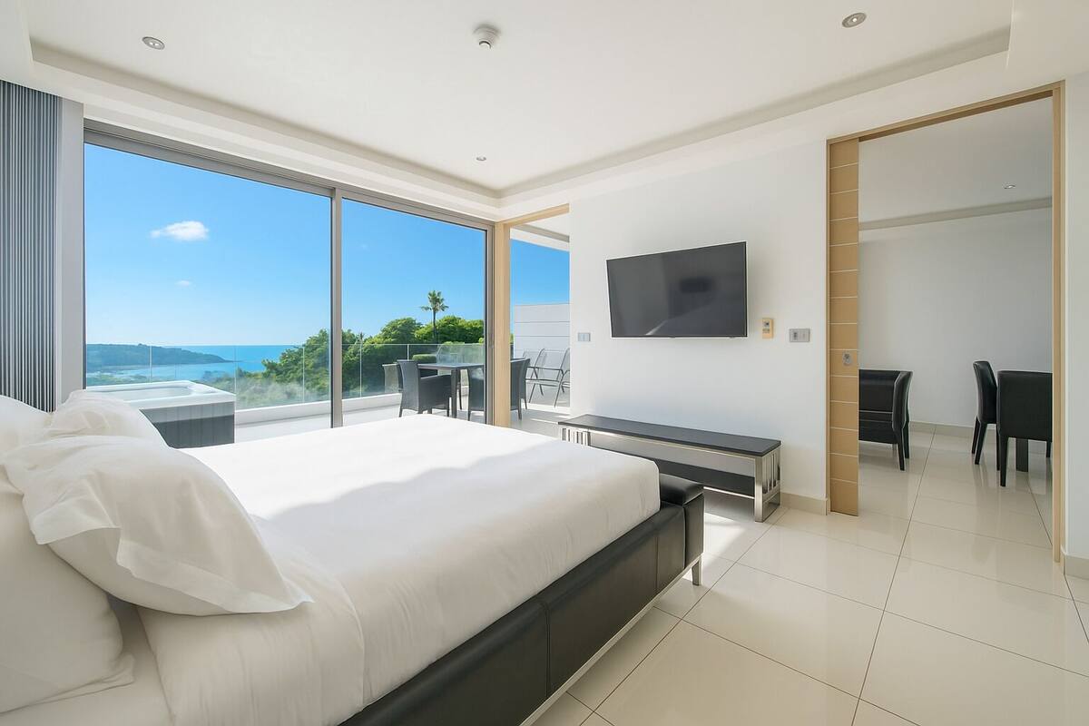 Una habitación de hotel moderna con una cama grande, televisor y balcón con vista al mar.