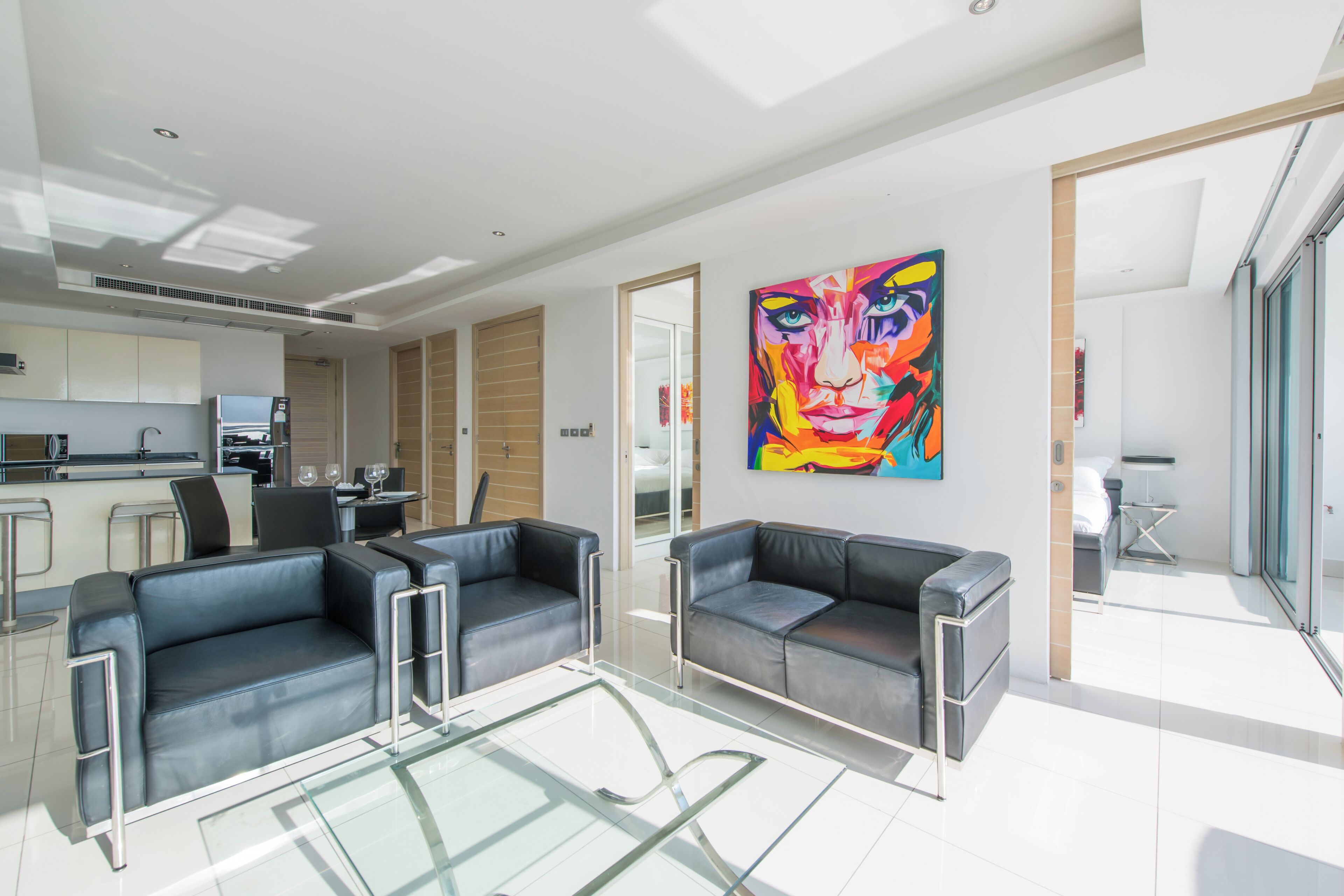 A modern living room with two black leather sofas, a glass coffee table, and a vibrant abstract painting on the wall.