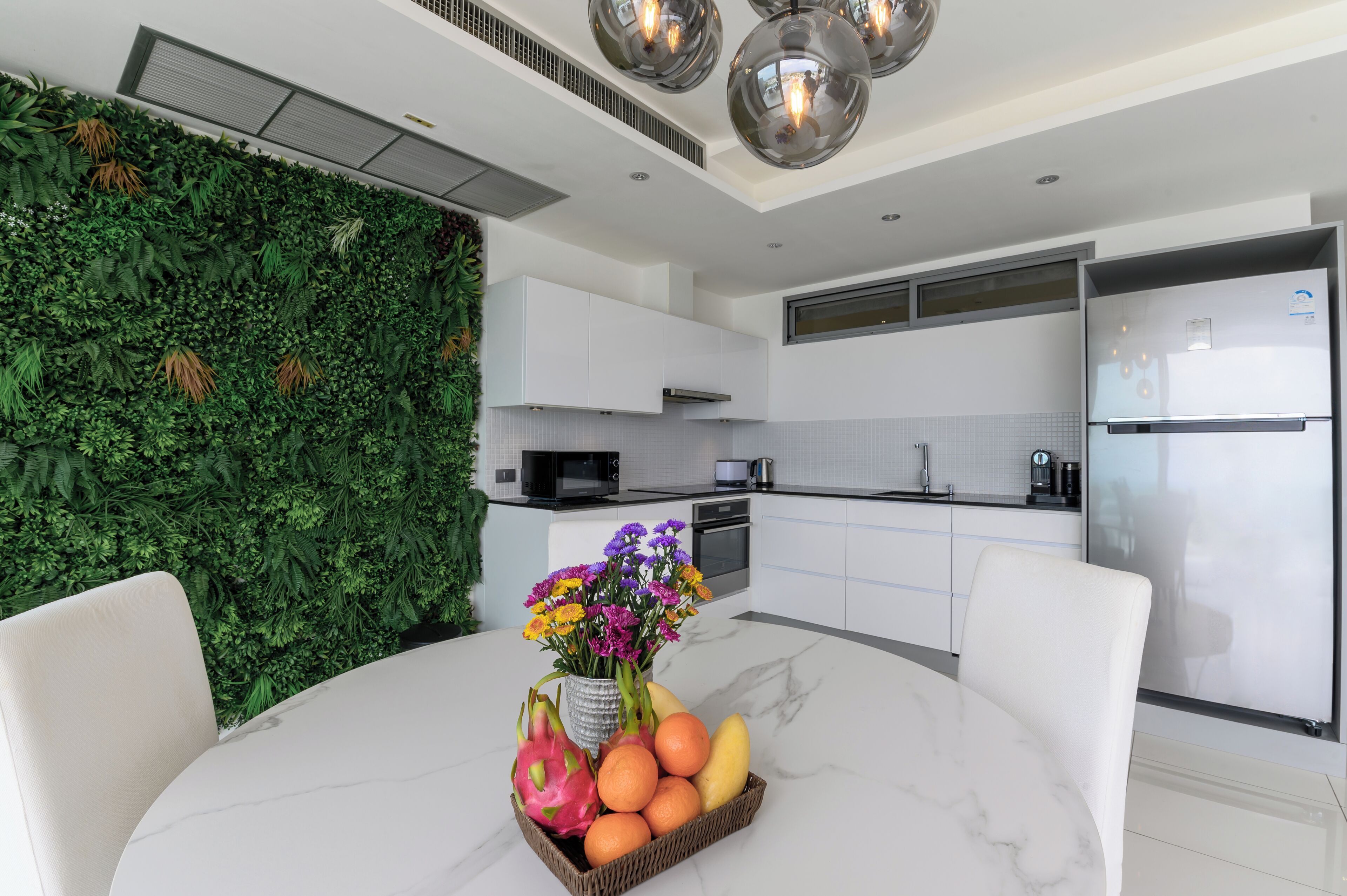A modern kitchen with white cabinets, a stainless steel refrigerator, and a green wall with plants.