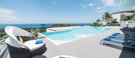 A poolside area with lounge chairs, a small table, and a view of the ocean.