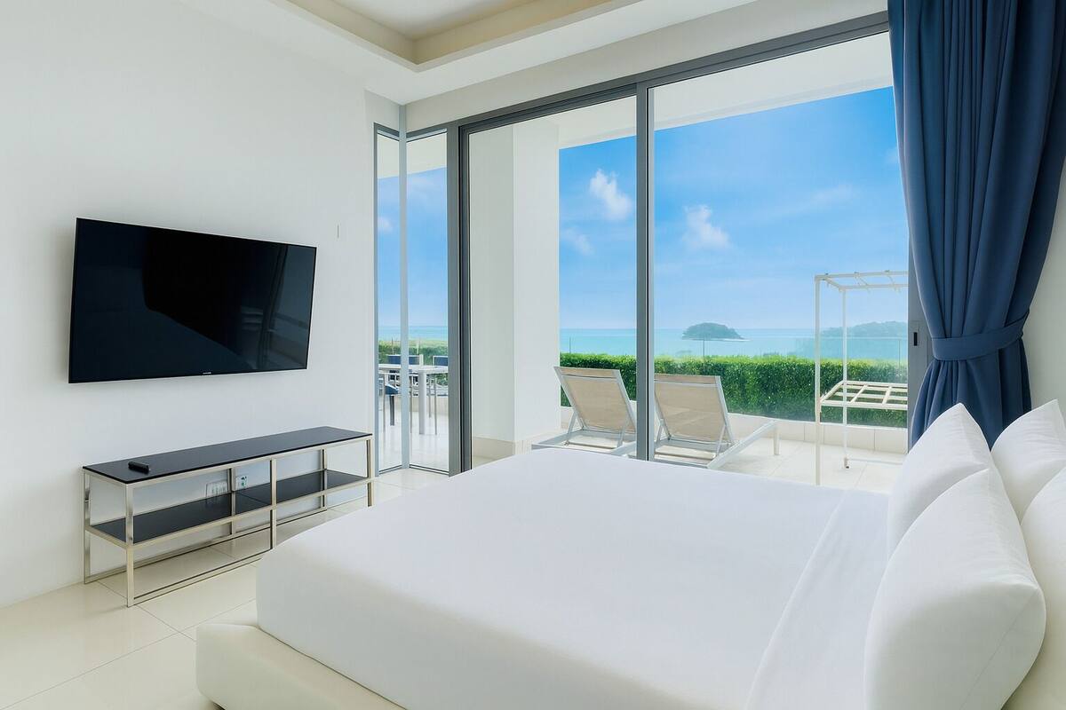 Una habitación de hotel moderna con una cama grande, un televisor de pantalla plana, un escritorio pequeño y un balcón con dos sillas.