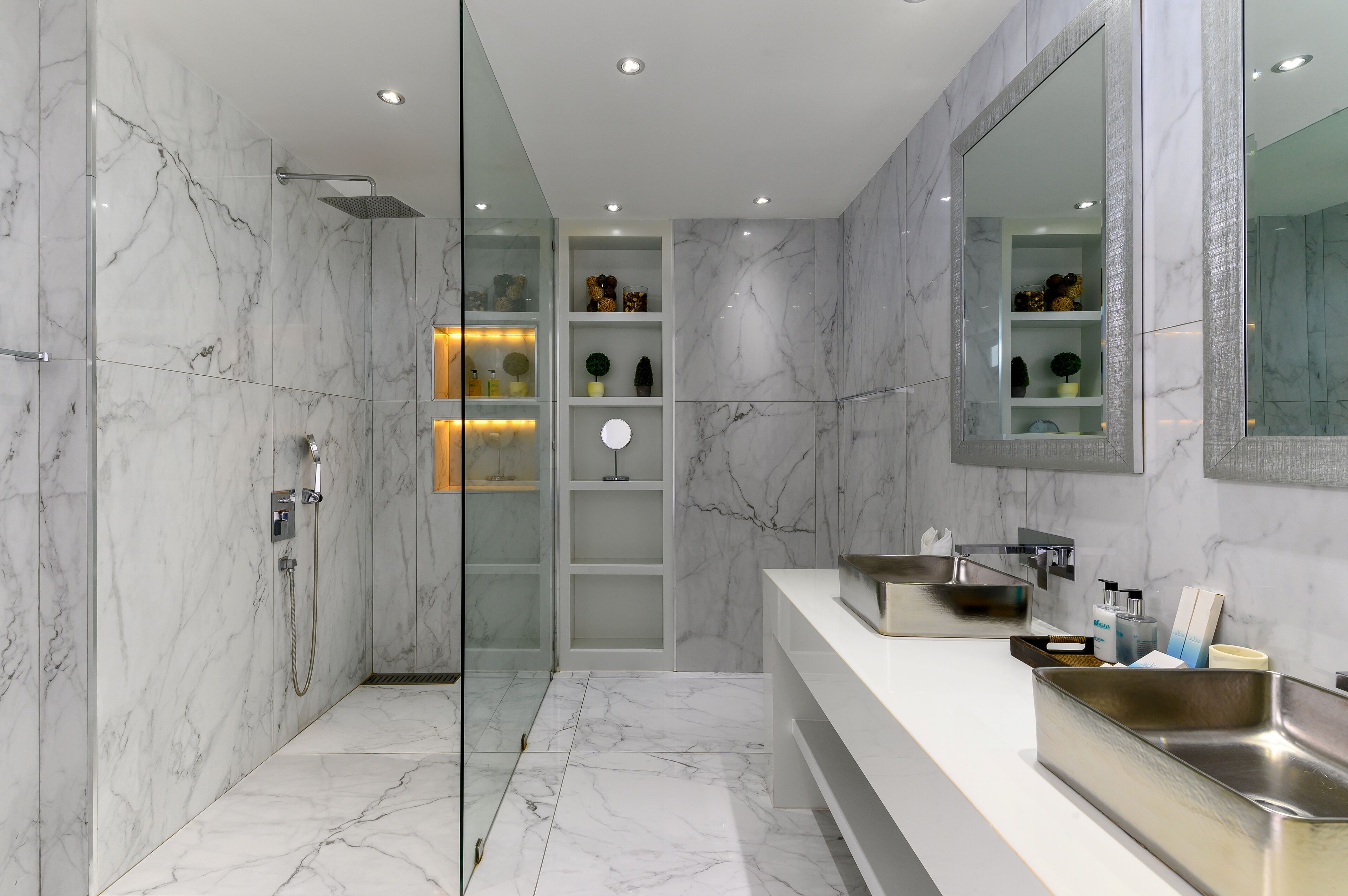 Un bagno moderno con pareti in marmo, cabina doccia in vetro e un mobile lavabo con un ampio specchio.