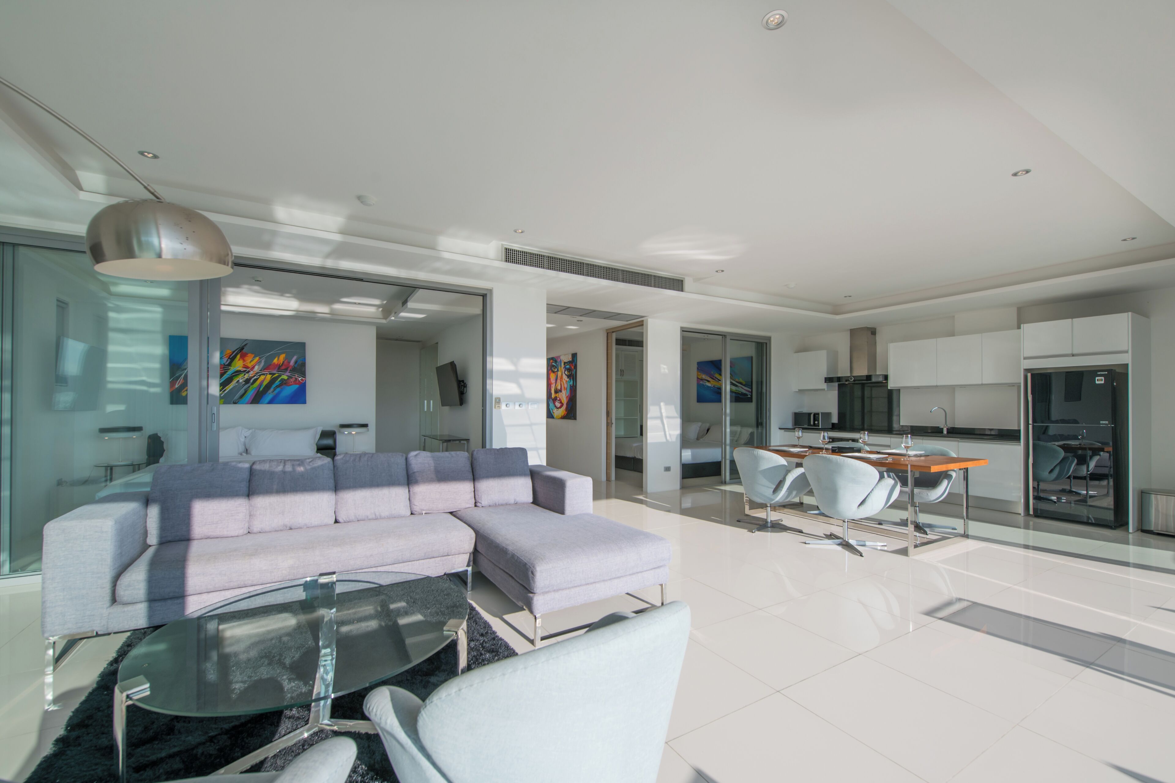 A modern living room with a sectional sofa, a glass coffee table, and a dining area with a white table and chairs.