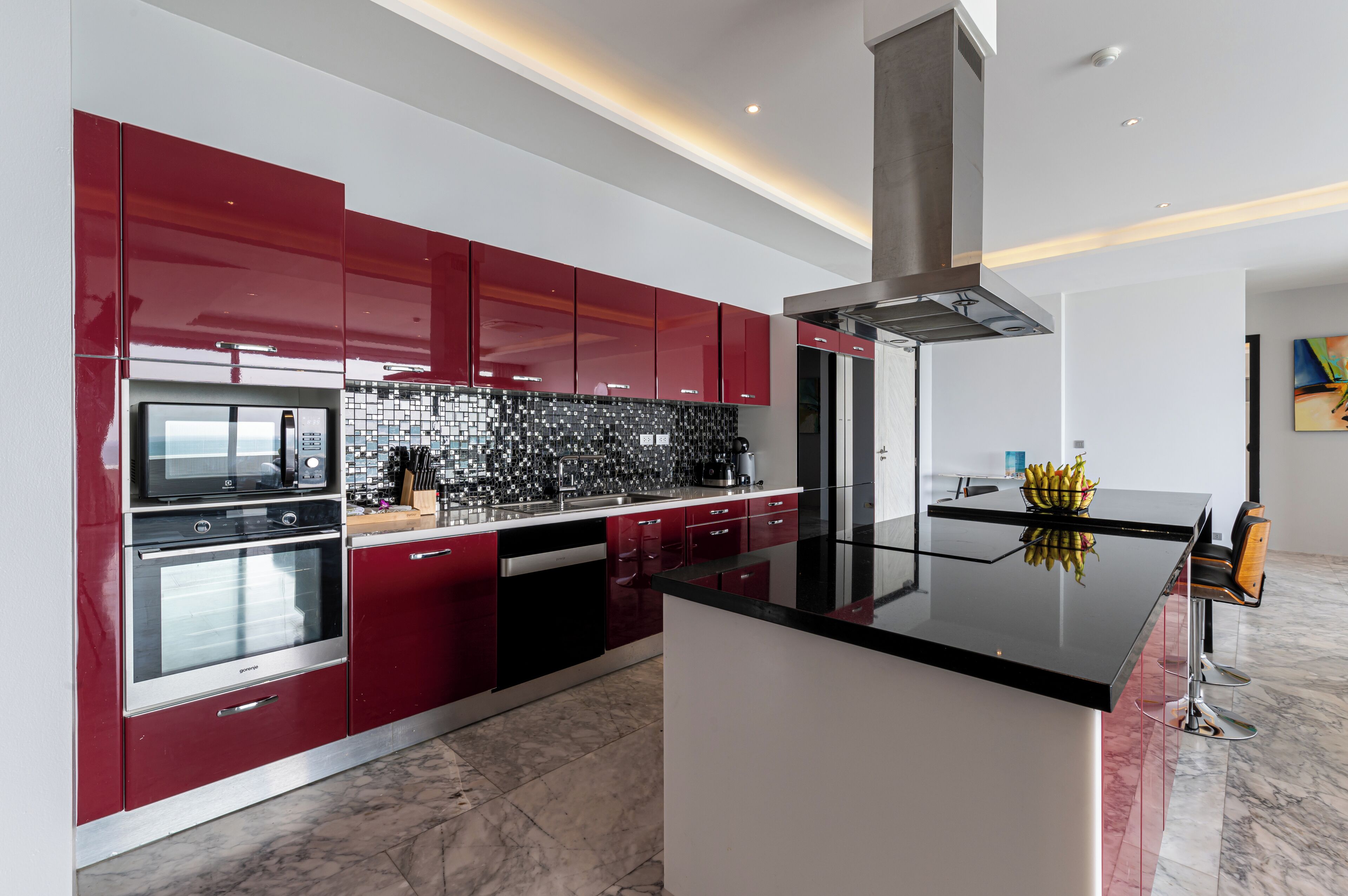 Una cocina moderna con gabinetes rojos, encimera negra y campana extractora de acero inoxidable.