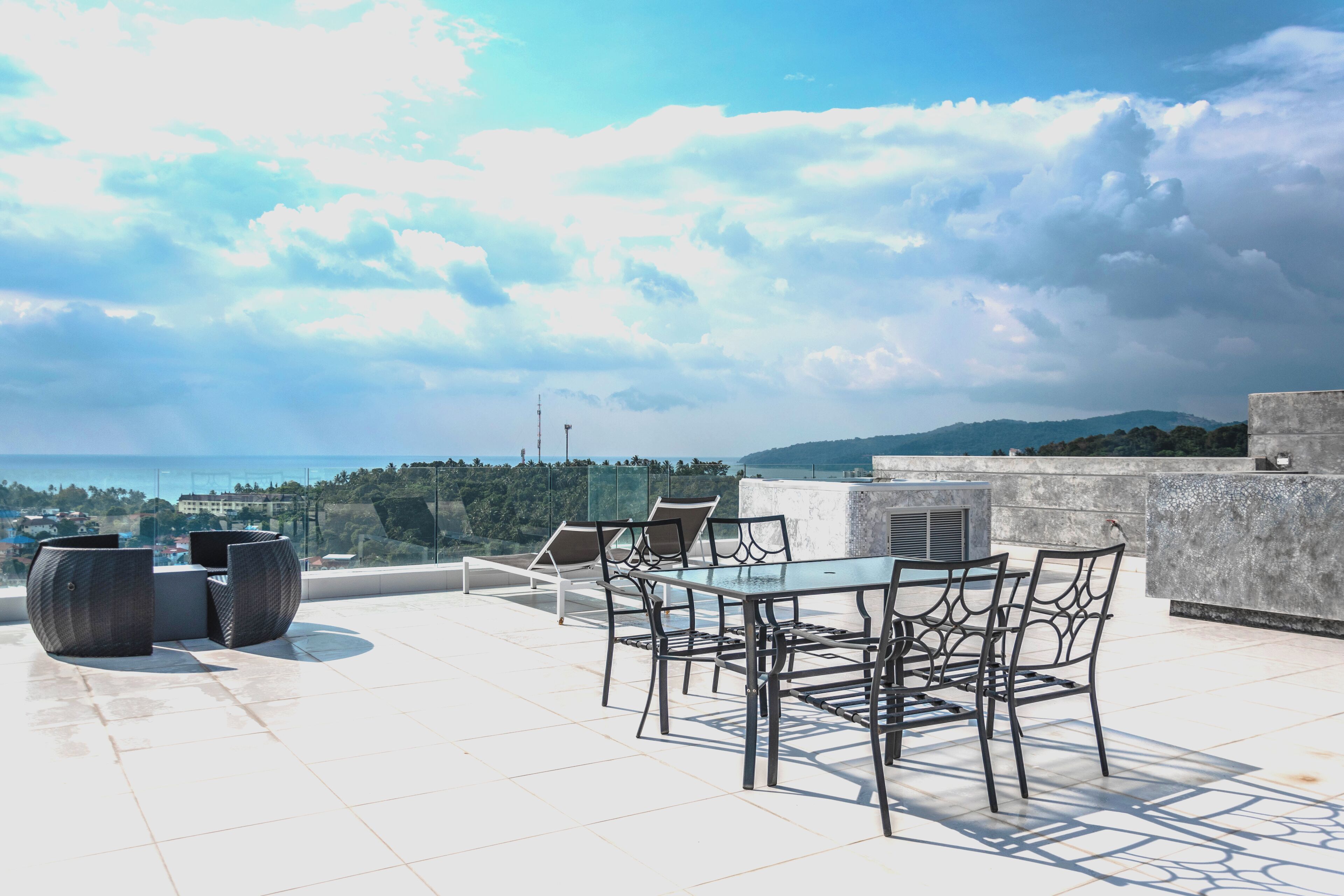 A rooftop terrace with a table and chairs, overlooking a scenic view of the sea and hills.