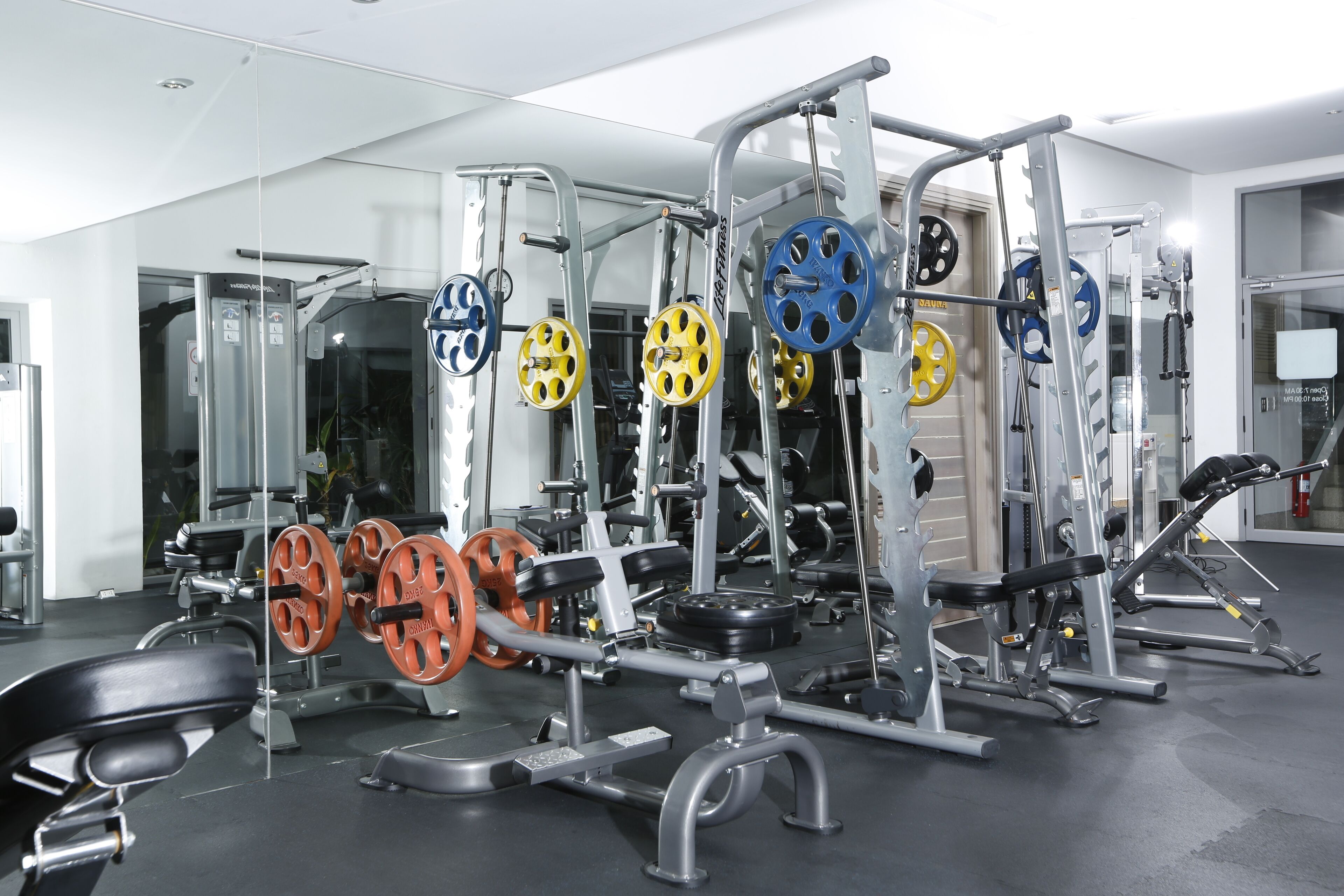 Ett gym med olika typer av styrketräningsutrustning, inklusive skivstänger, viktskivor och träningsmaskiner.