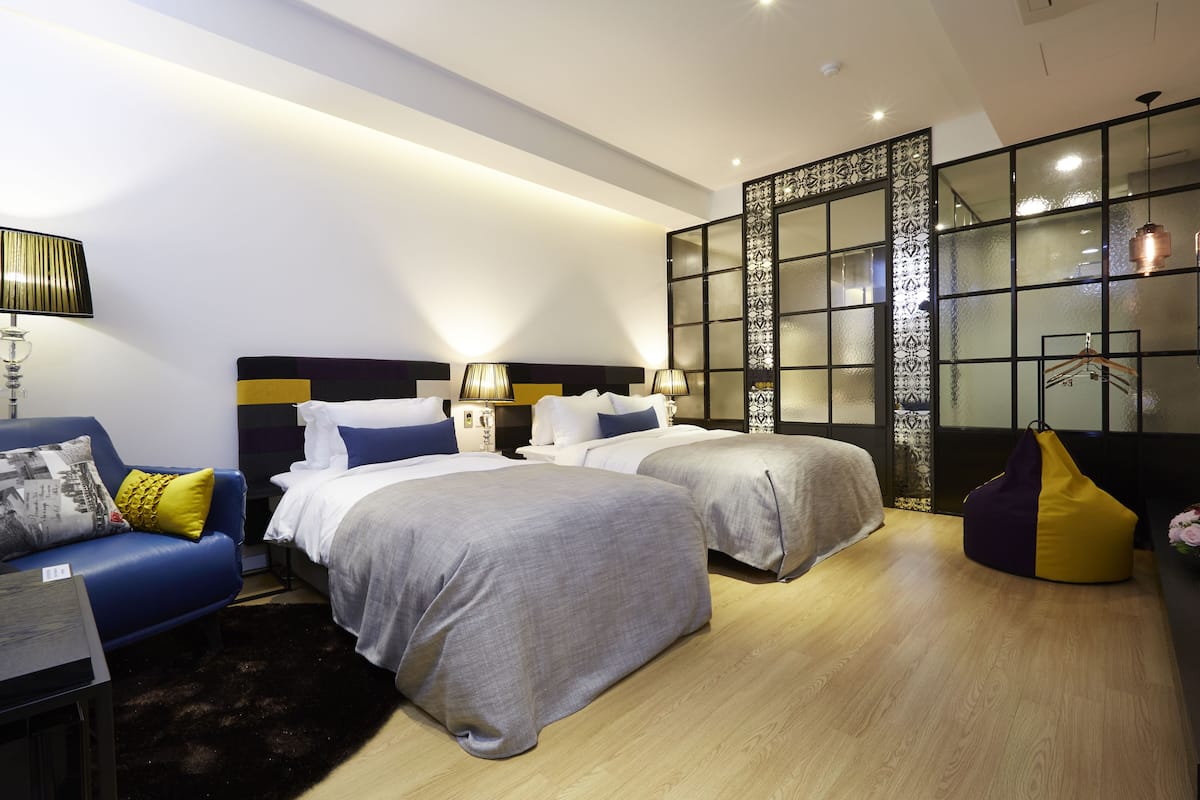 Un dormitorio moderno con dos camas, un sofá, un muro decorativo y una lámpara colgante.