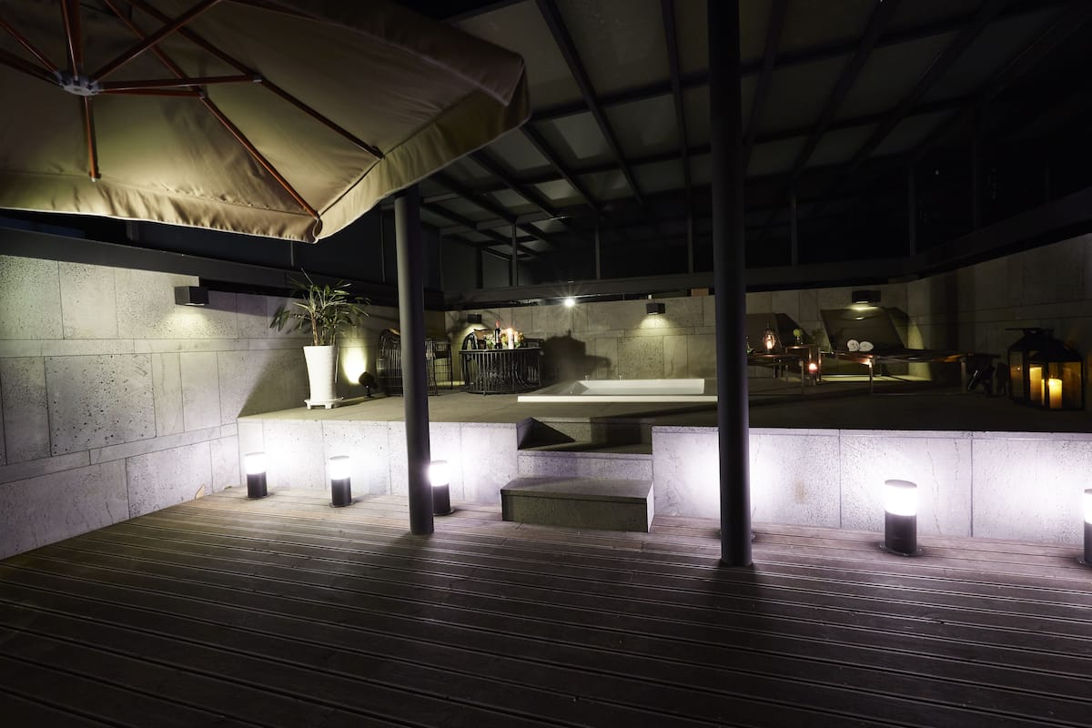 Un patio exterior con zona de estar cubierta, escalones e iluminación ambiental.