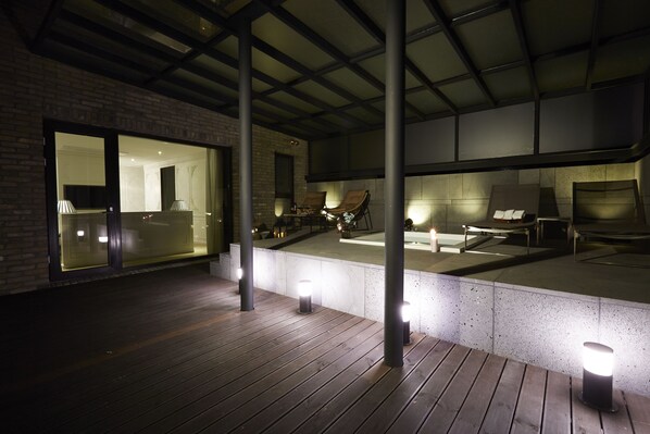 Terraza exterior con piso de madera y zonas de estar, iluminada por luces en el suelo.