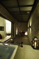 Um quarto acolhedor, com iluminação suave, uma banheira grande, uma mesa de jantar com cadeiras e um espaço de estar confortável com almofadas.