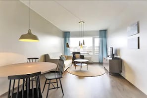 Un salon moderne avec une table de salle à manger ronde, des chaises noires, un canapé et un téléviseur.