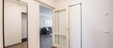 Un pasillo con piso de madera, un espejo grande y un vidrio corredero que da a un área de estar con un sofá y una mesa de centro.