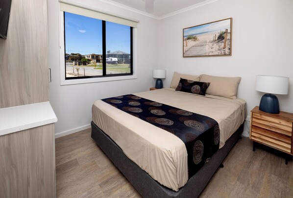 A bedroom with a large bed, two bedside tables, a window with a view, and a painting on the wall.