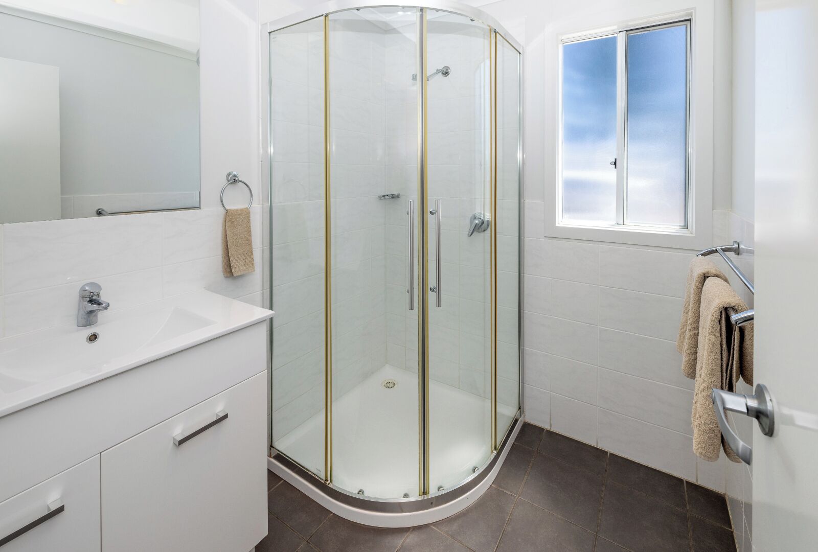 Een moderne badkamer met een douchecabine van glas, een witte wastafel en een raam met uitzicht.
