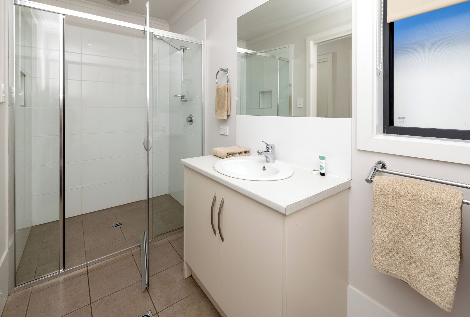 A modern bathroom with a glass shower enclosure, a white sink, and a large mirror.