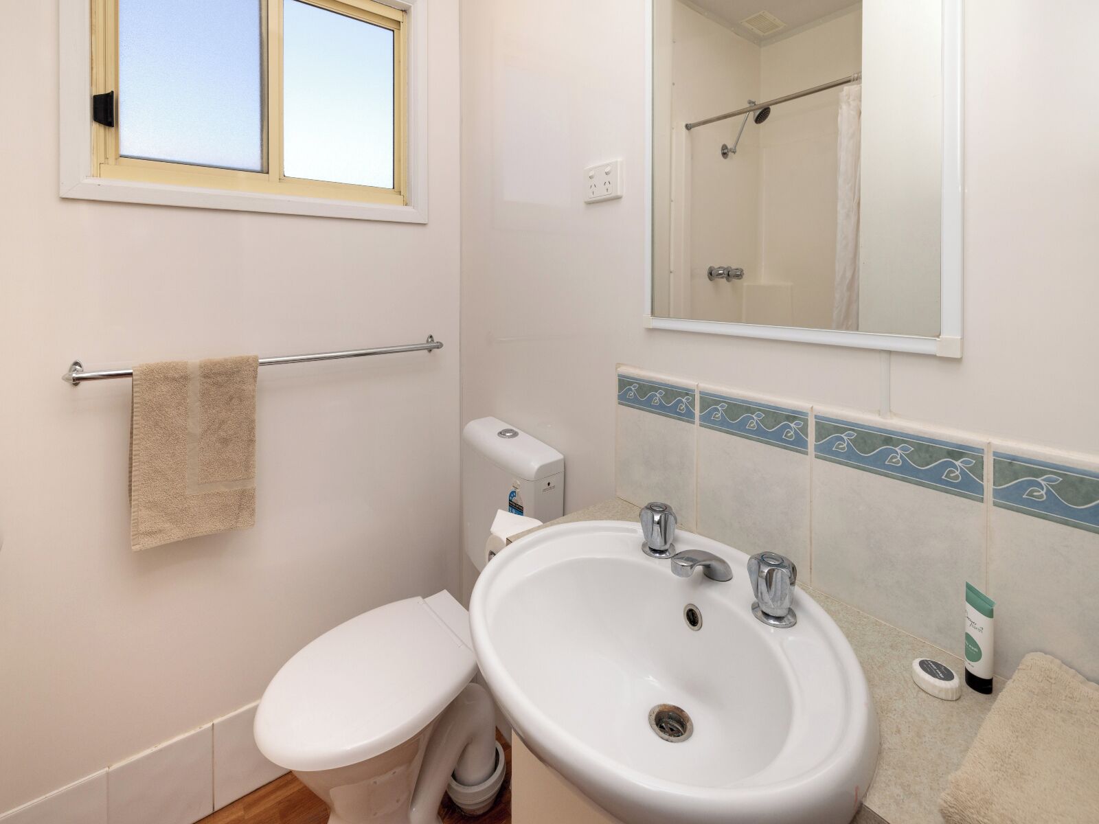 A bathroom with a toilet, sink, towel rack, and a window.