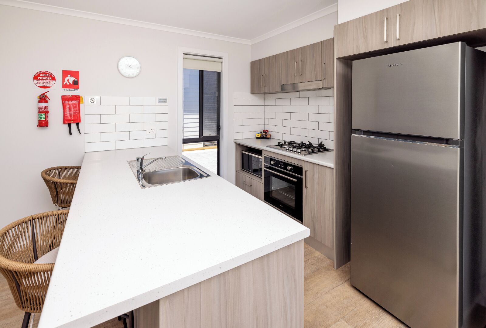 A modern kitchen with white countertops, stainless steel appliances, and light wood cabinets.