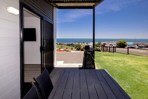 An outdoor patio with a view of the sea, a barbecue grill, and a paved area with cars. - BIG4 Port Hughes Holiday Park (Port Hughes)