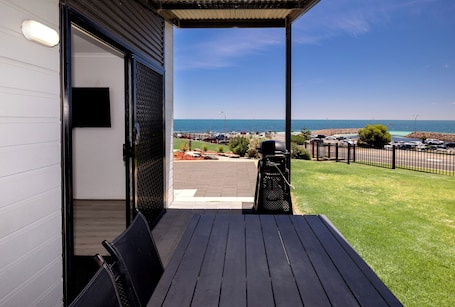 An outdoor patio with a view of the sea, a barbecue grill, and a paved area with cars.. BIG4 Port Hughes Holiday Park