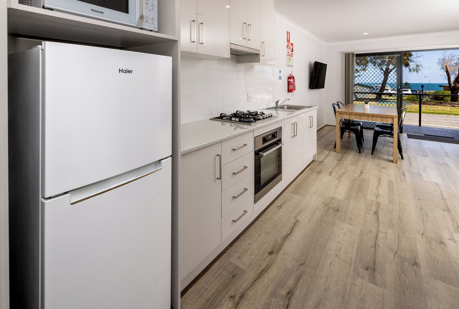 Une cuisine moderne avec des meubles blancs, un four encastré, une cuisinière à gaz et un four à micro-ondes.