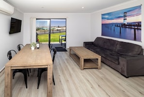 A modern living room with a wooden dining table, a sofa, and a painting of a lighthouse.