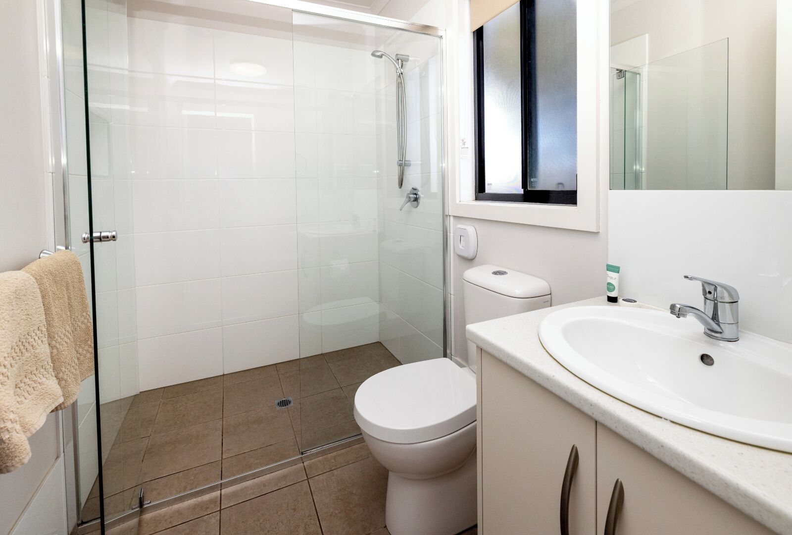 A modern bathroom with a glass shower enclosure, a white toilet, and a sink with a mirror above.