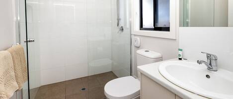 A modern bathroom with a glass shower enclosure, a white toilet, and a sink with a mirror above.