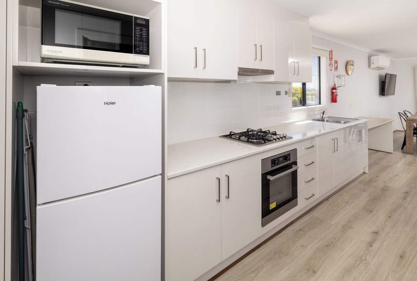 Una cocina moderna con armarios blancos, un microondas, un refrigerador, una estufa a gas y un horno.