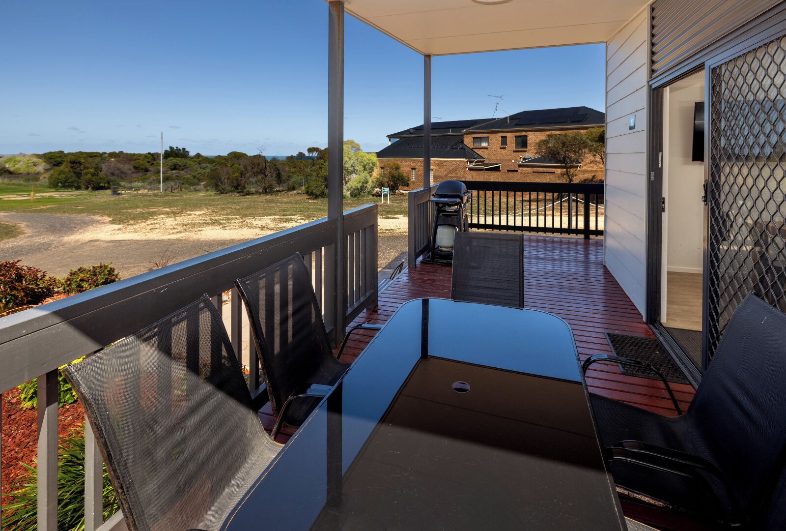 A balcony with a table and chairs, a view of the landscape, and a building in the background.