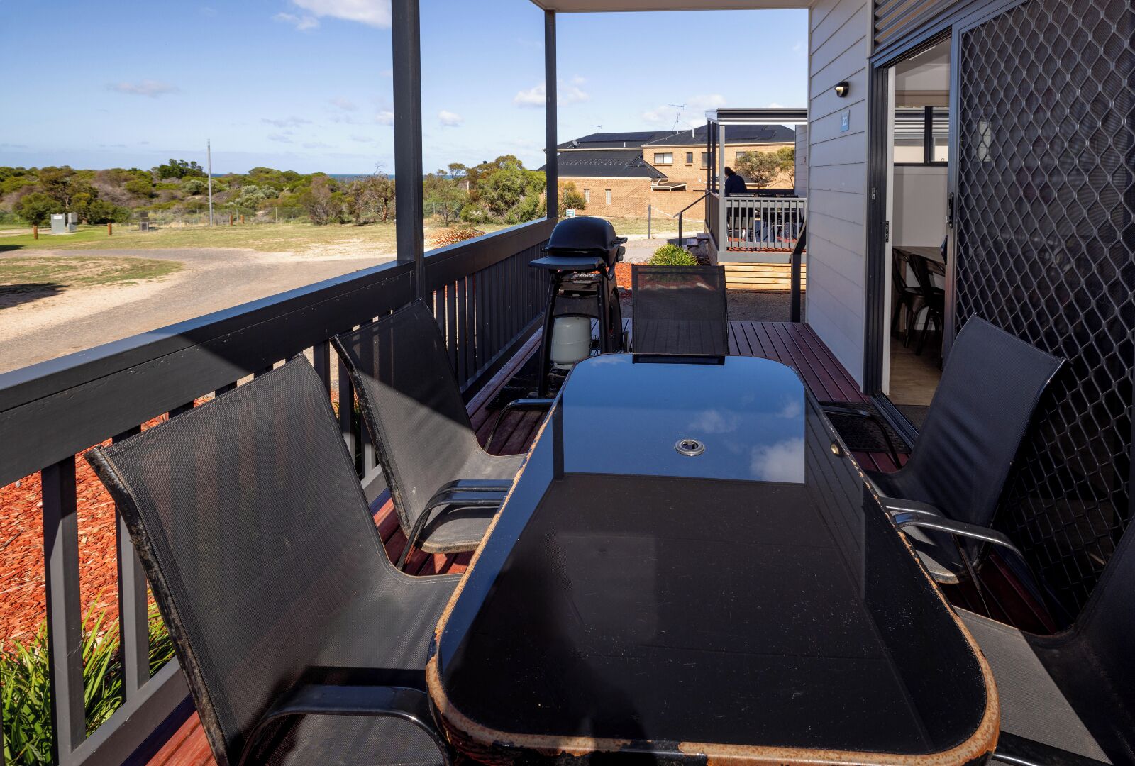 A covered outdoor patio with a table and chairs, a grill, and a view of the surrounding area.
