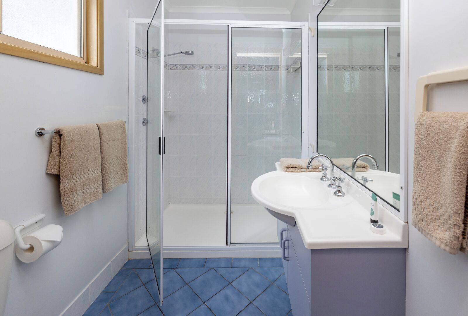 A modern bathroom with a glass shower enclosure, a white sink with a mirror, and a blue-tiled floor.