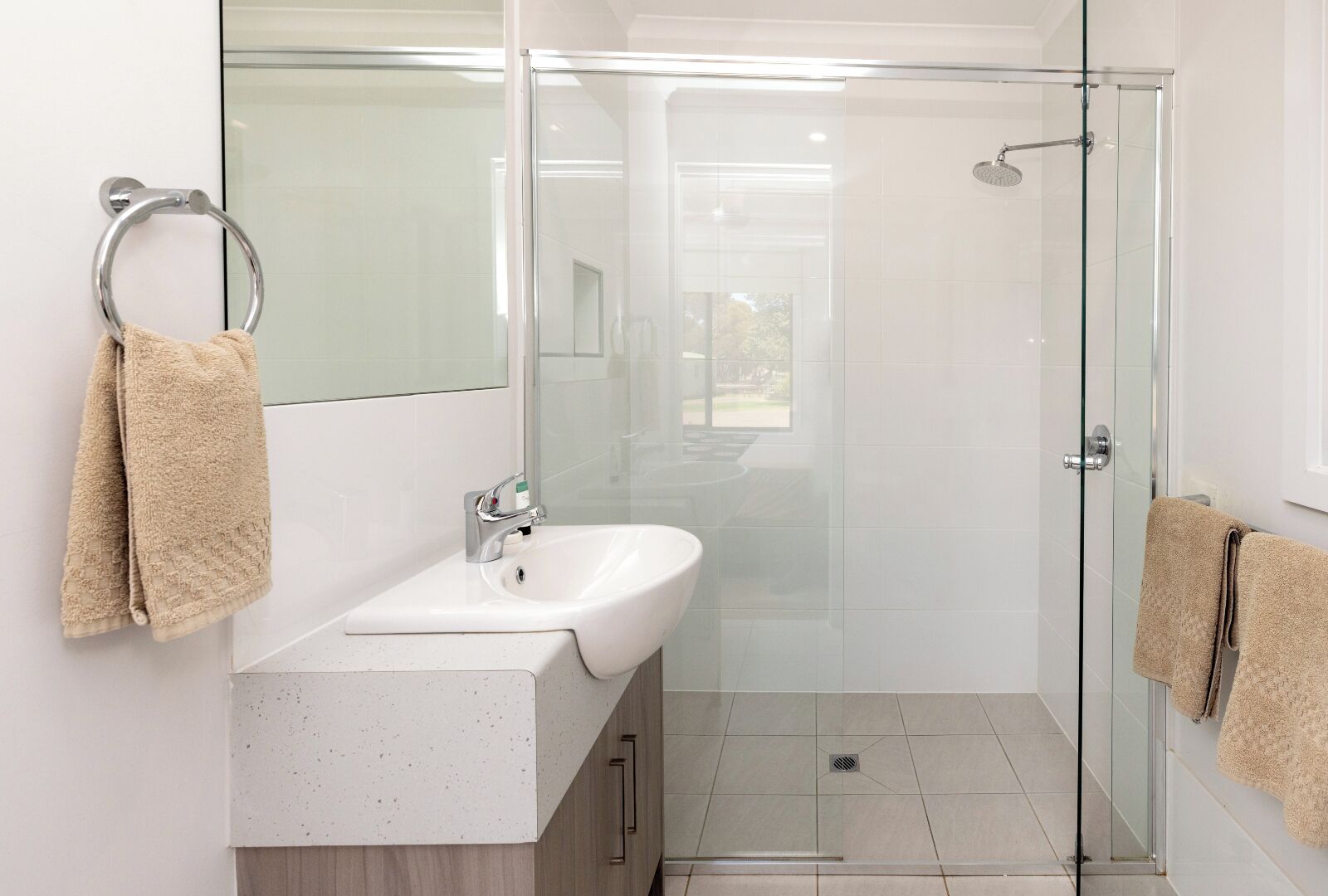 Un baño moderno con cabina de ducha de vidrio, un lavamanos blanco y dos toallas.