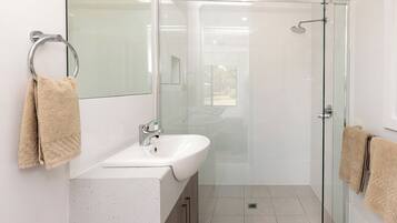 Un baño moderno con cabina de ducha de vidrio, un lavamanos blanco y dos toallas.