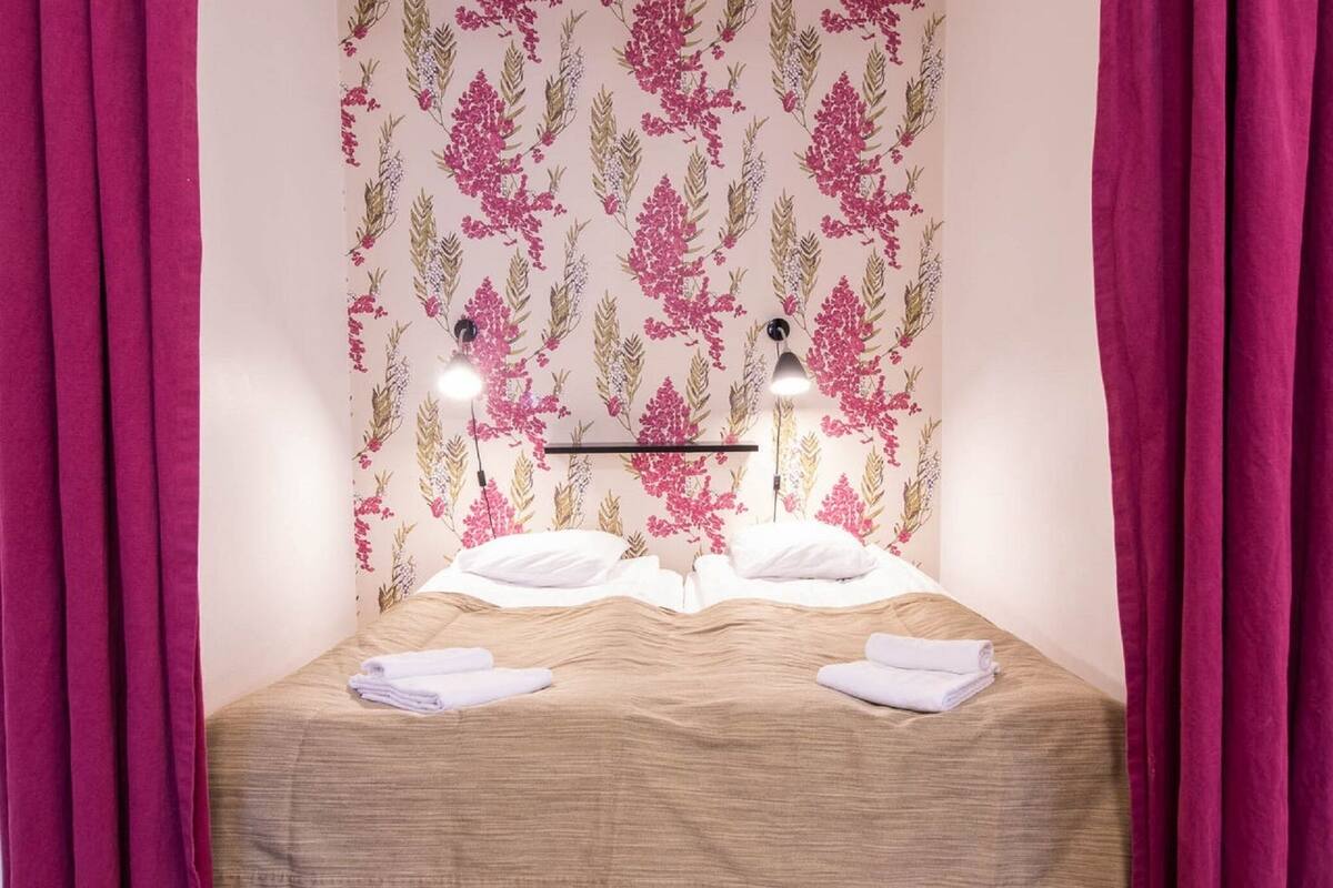A neatly made bed with white linens, two bedside lamps, and a floral wallpaper pattern.