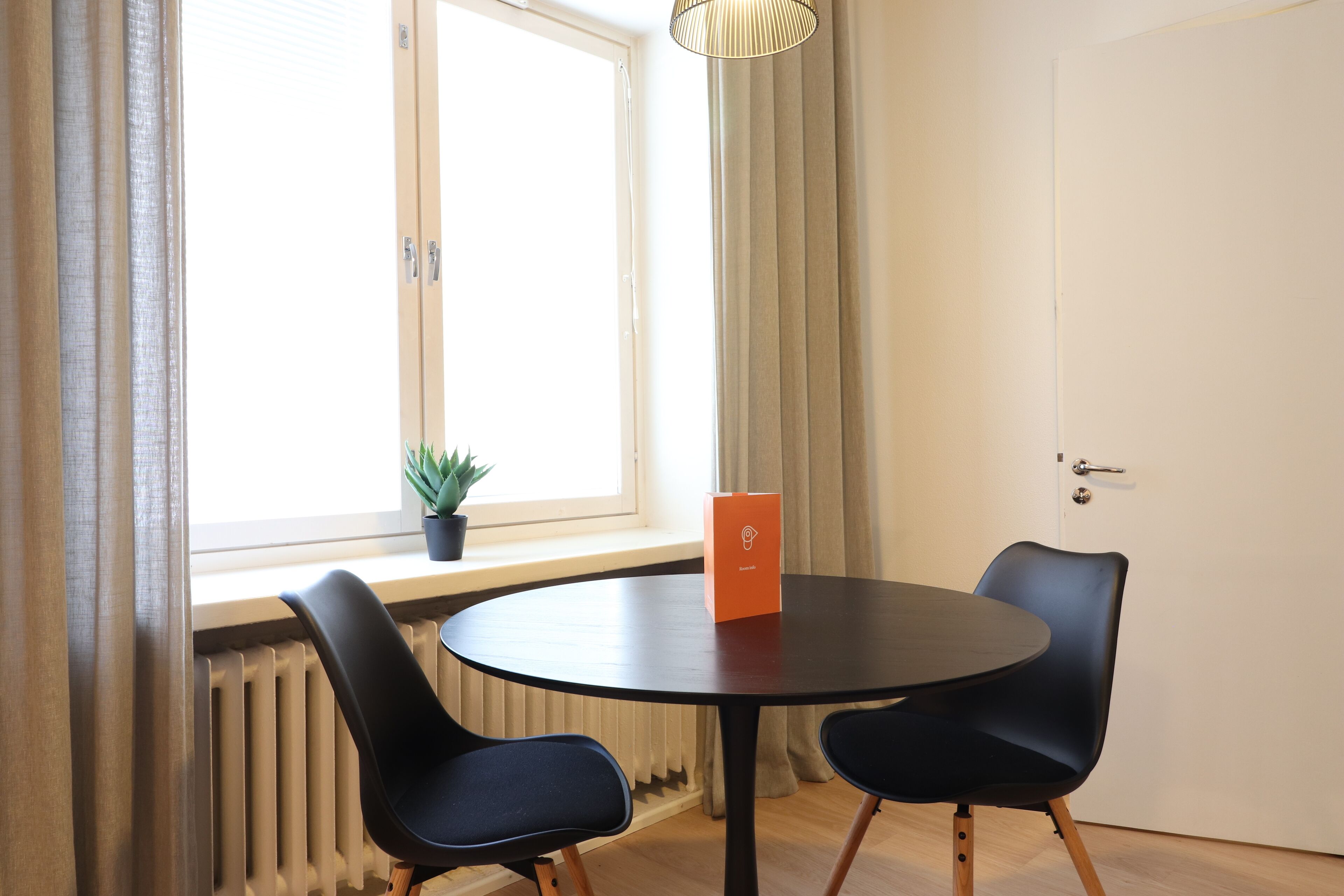 A room with a round table, two chairs, a potted plant, and a door.