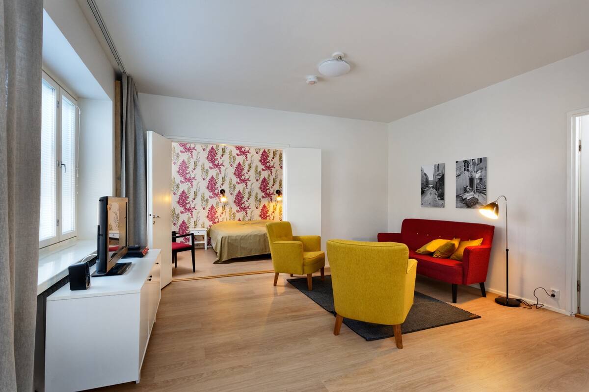 A modern living room with a bed, yellow armchairs, a red sofa, and a dining area.