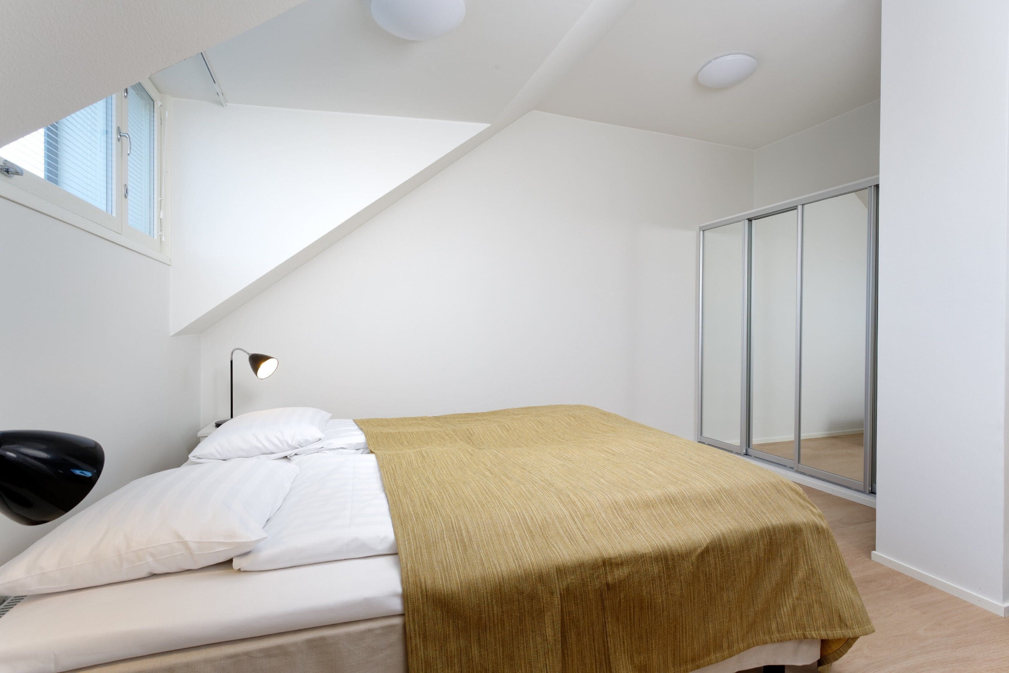 Ein Schlafzimmer mit Bett, Nachttischlampe, Fenster und einer Schiebetür.