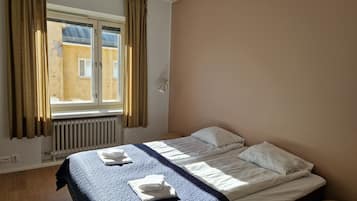 A hotel room with a bed, a window with curtains, a radiator, and a small table.