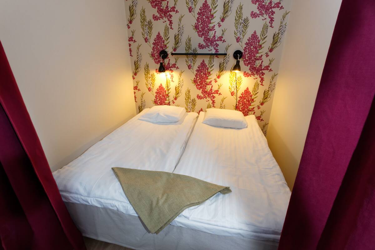 A single bed with white linens, a beige throw blanket, and a floral wallpaper pattern.