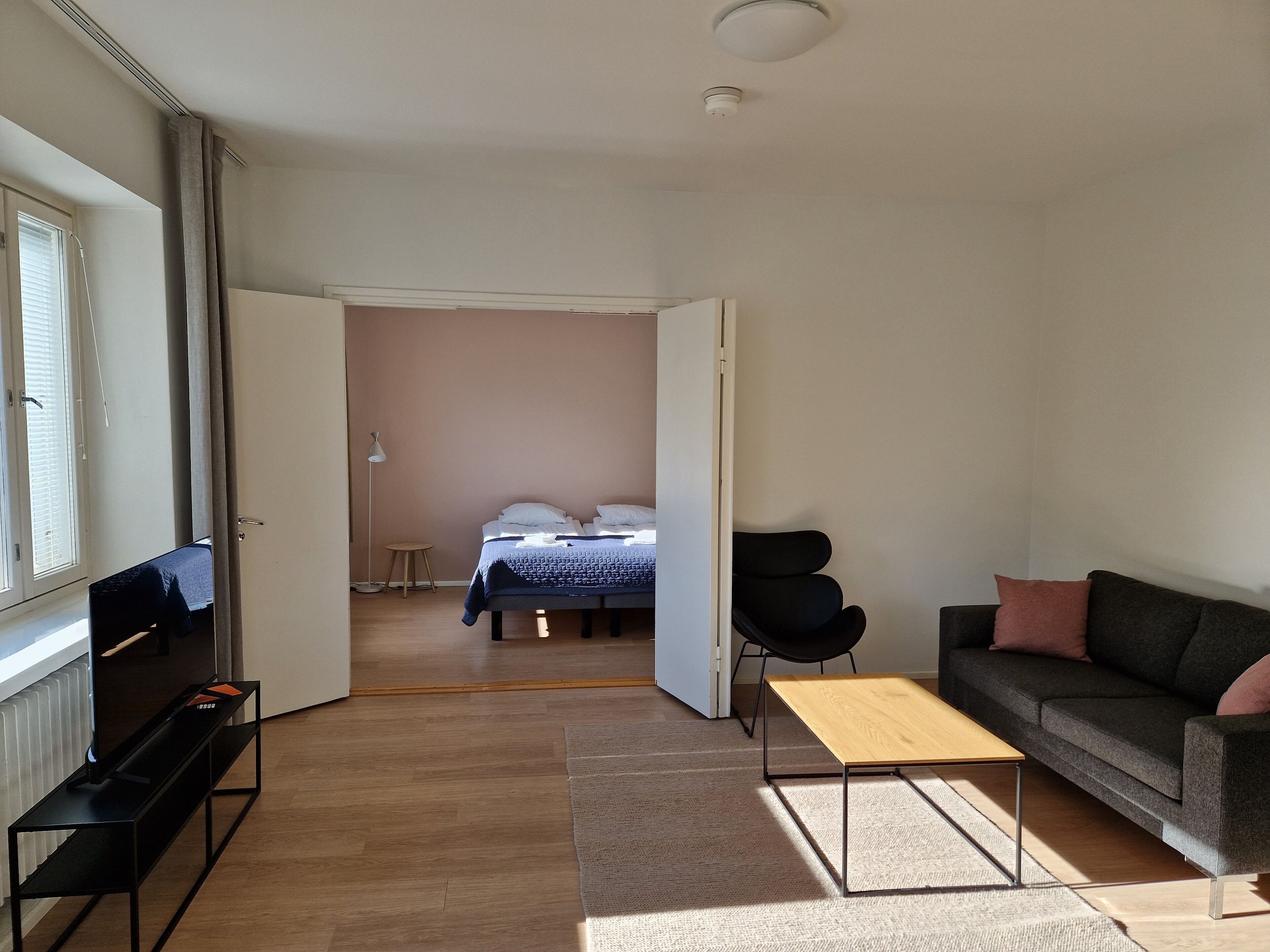 Et moderne hotelværelse med seng, sofa, fjernsyn på et stativ og et lille bord.