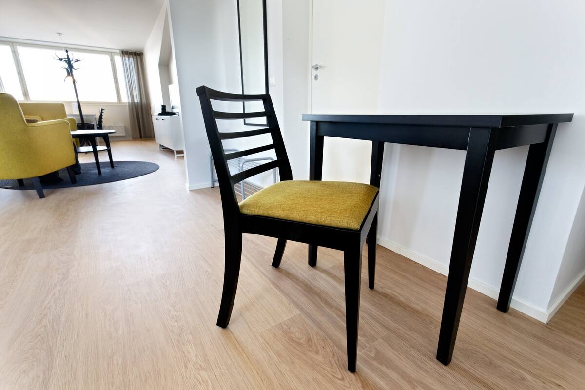 A modern living room with a wooden floor, a black table, a yellow armchair, and a black chair with a yellow cushion.